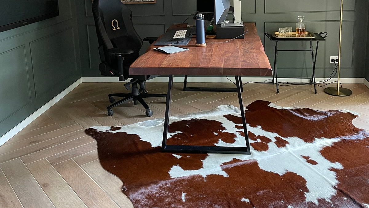 Brown and white cowhide rug under a timber desk in a green study